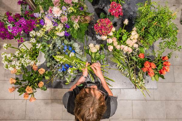 Du siehst eine Floristin im Raiffeisen-Markt, die aus bunten Schnittblumen einen Strauß arrangiert.