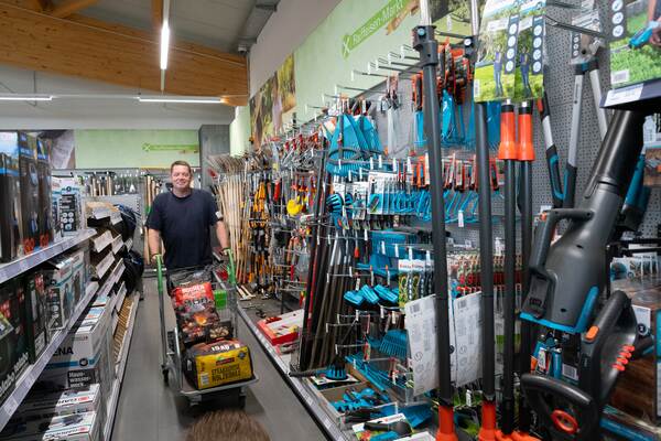 Du siehst ein Regal mit blauen Gardena-Gartengeräten wie Rechen, Scheren und Teleskopstielen.