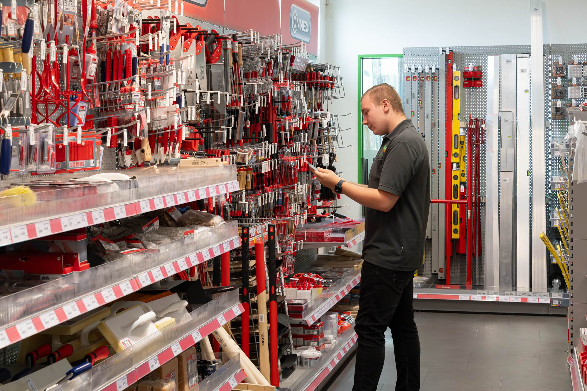 Kunde betrachtet Handwerkzeuge in einem Baumarktregal mit Zangen, Sägen und Wasserwaagen.