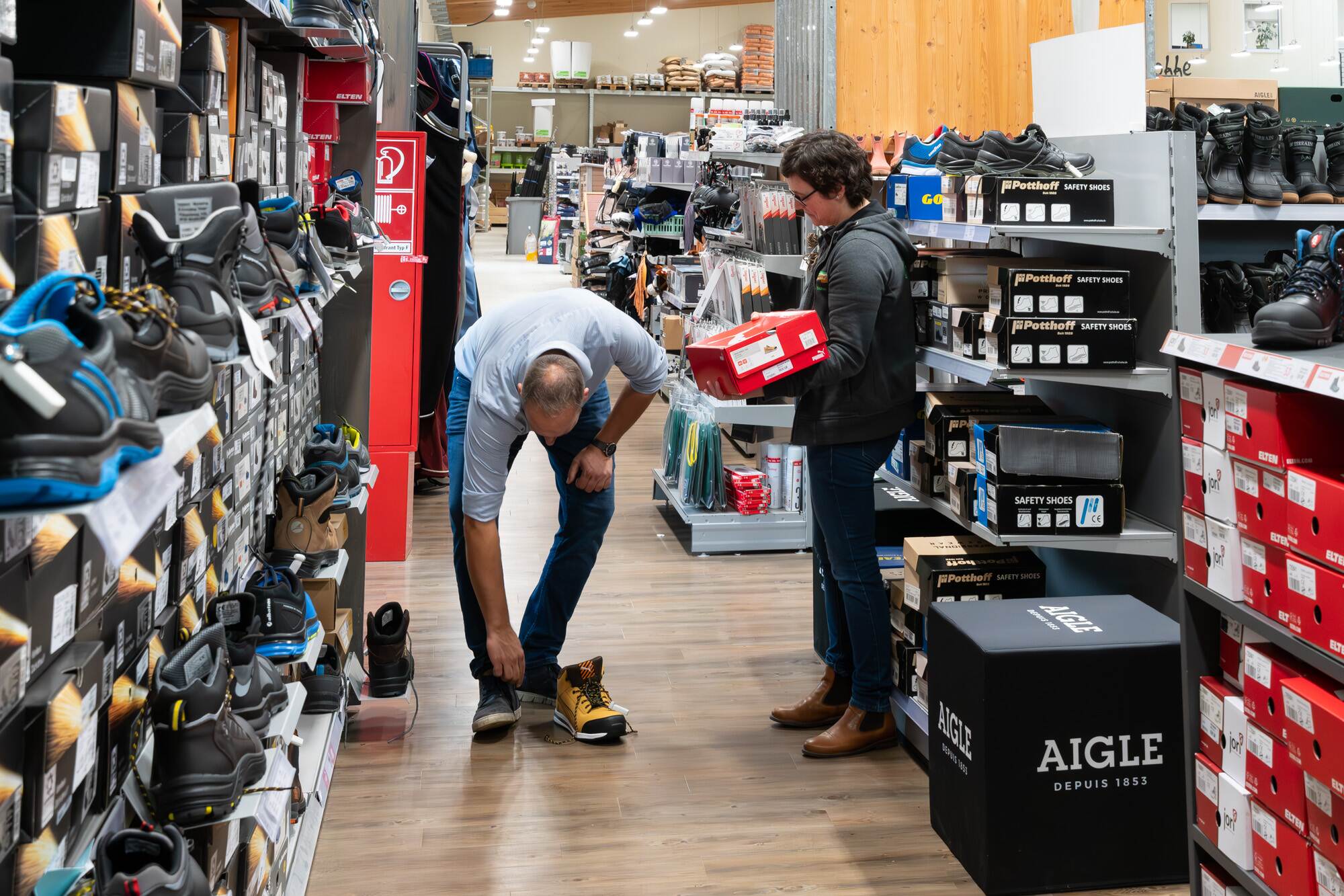 Du siehst zwei Personen im Raiffeisen-Markt, die Sicherheitsschuhe auswählen und ein Paar zum Anprobieren bereitlegen.
