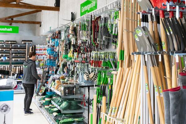 Du siehst ein Regal im Raiffeisen-Markt mit Gartengeräten, Spaten, Rechen, Hacken und weiterem Zubehör.