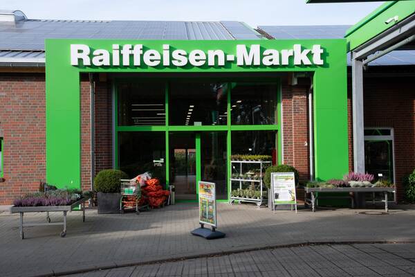 Du siehst den Eingangsbereich vom Raiffeisen Markt Fredenbeck mit Pflanzen und Werbetafeln im Außenbereich.