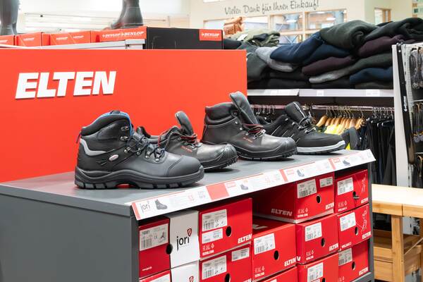 Du siehst eine Verkaufsfläche mit Sicherheitsschuhen der Marke Elten auf roten Kartons im Raiffeisen-Markt.