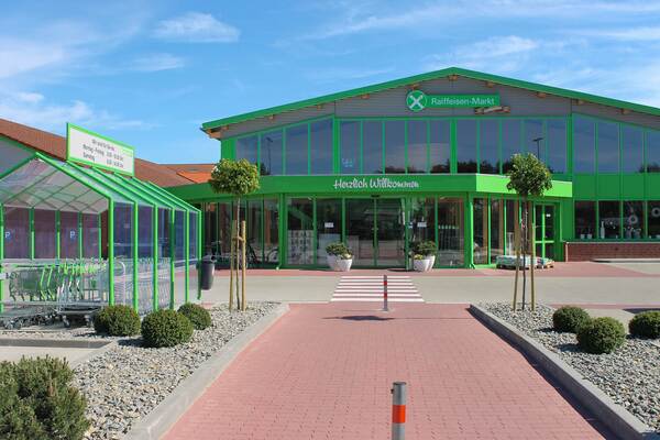 Moderner Raiffeisen-Markt mit großem Glasfassadeneingang, grünem Rahmen und überdachtem Bereich für Einkaufswagen.