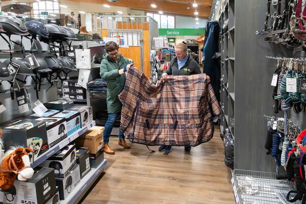 Zwei Frauen halten in einer Reitsportabteilung eine große karierte Pferdedecke und begutachten sie gemeinsam.