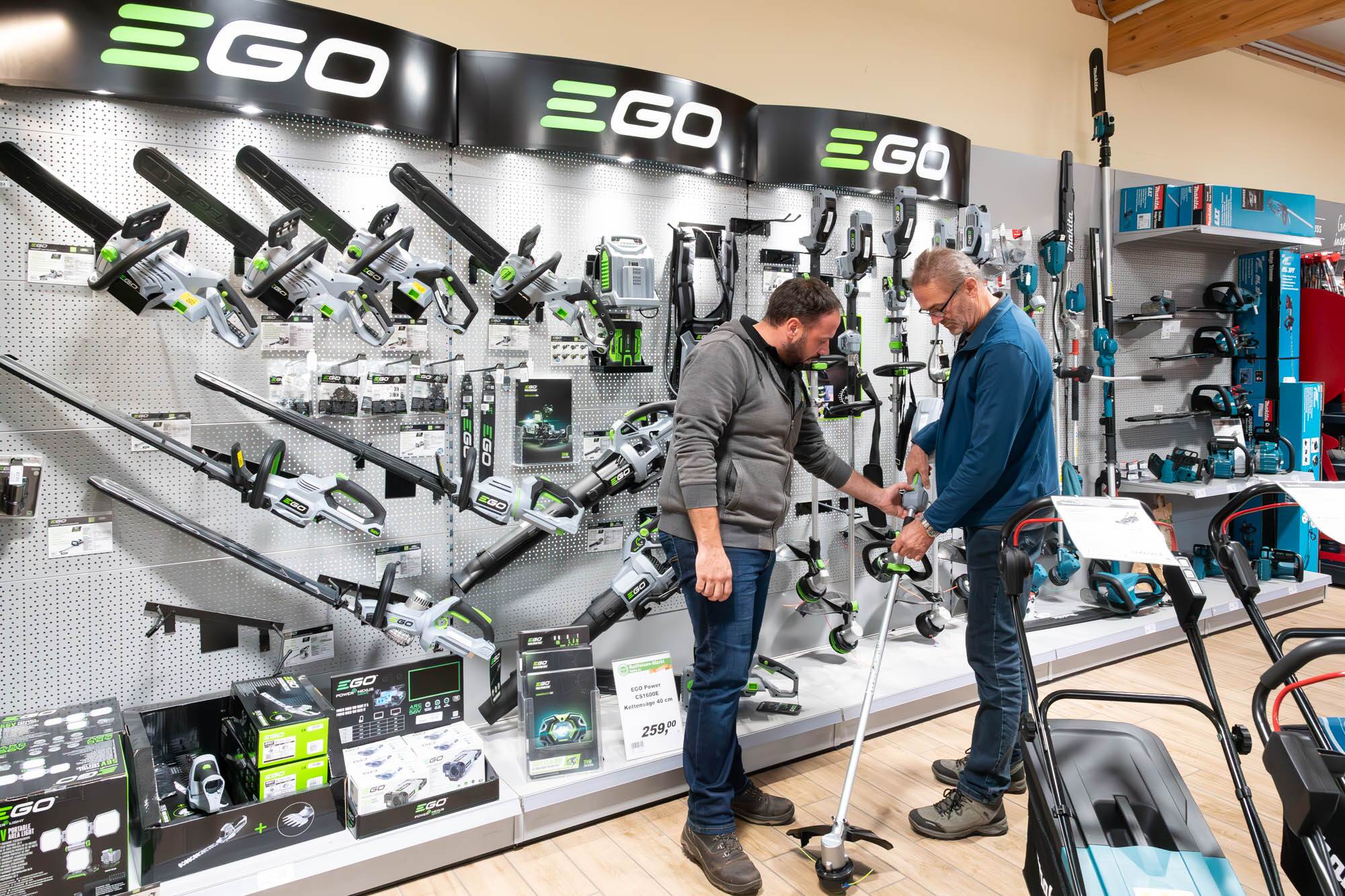 Du siehst eine Auswahl an EGO Gartengeräten im Raiffeisen-Markt, darunter Kettensägen und Rasentrimmer.