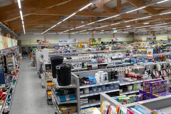 Du siehst einen großen Baumarkt mit Regalen voller Haushaltsartikel, Werkzeug und Tierbedarf unter Holzdecke.